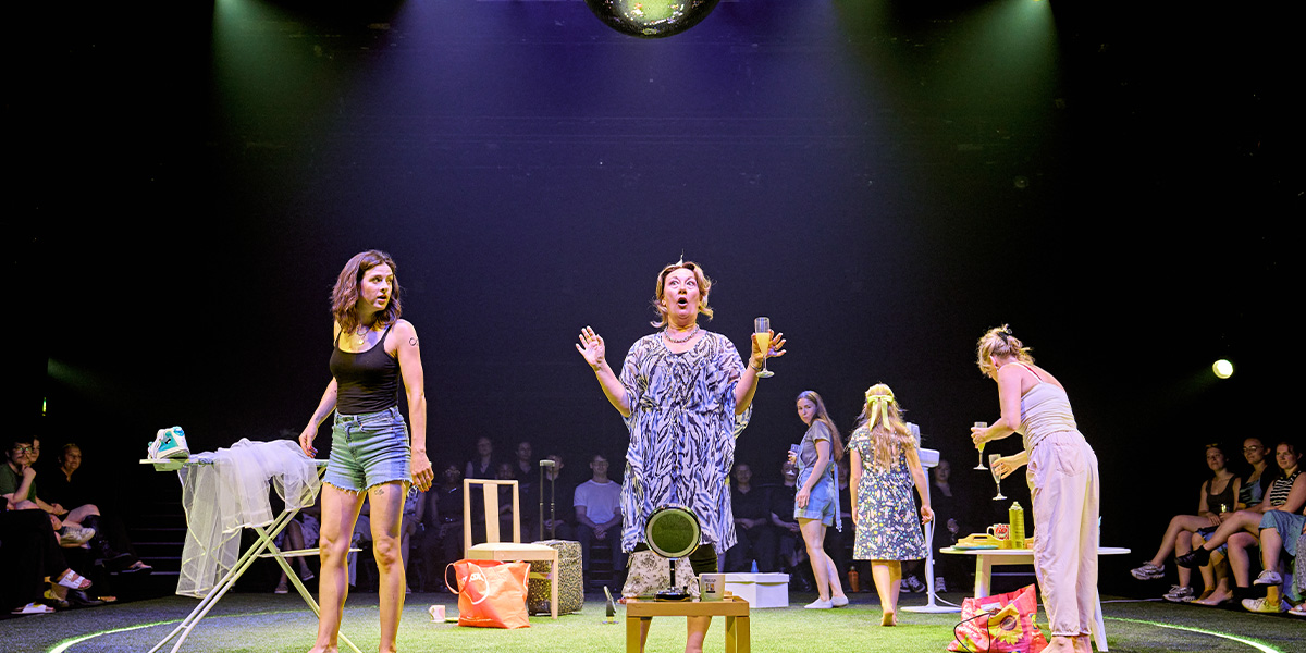 A lively theatrical scene with multiple performers on stage under a bright spotlight and a disco ball, engaging actively with the audience.