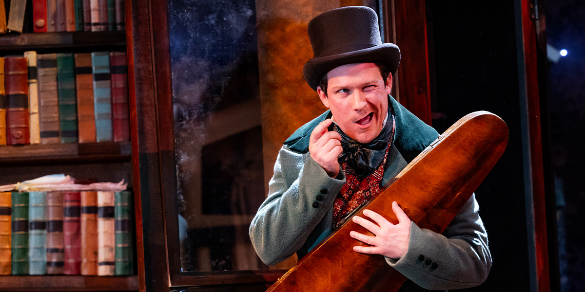 Matt Cavendish performing on stage in a festive costume, surrounded by Christmas decorations and stage lights.