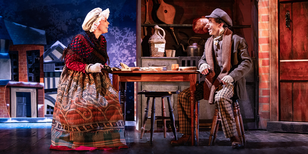 Sasha Frost and Jonathan Sayer pose together, smiling, in festive costumes from "Christmas Carol Goes Wrong.