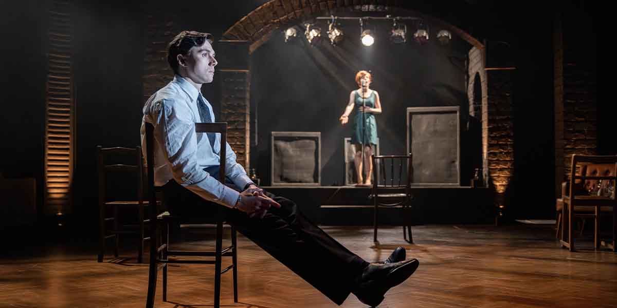 Calam Lynch sits on a chair, while Eleanor Worthington-Cox performs on stage in a green dress.