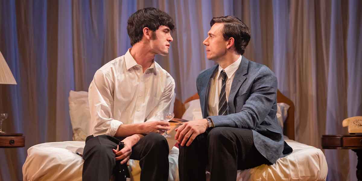 Noah Ritter and Calam Lynch sit closely on a bed, engaged in an intense conversation.