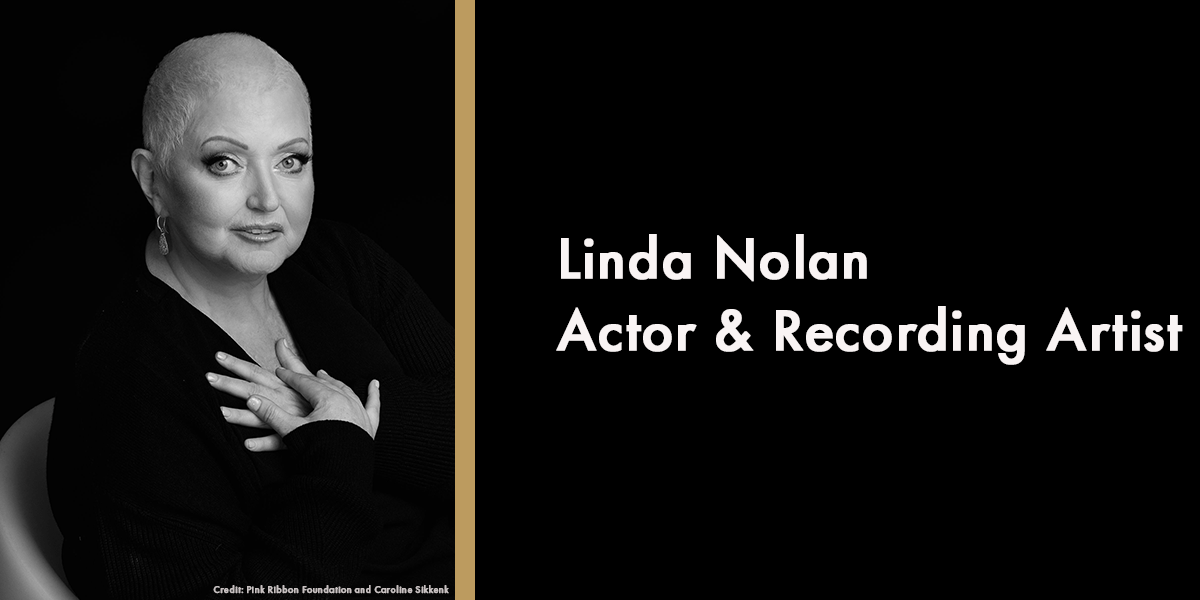 A woman with short hair poses in a black outfit against a dark background.