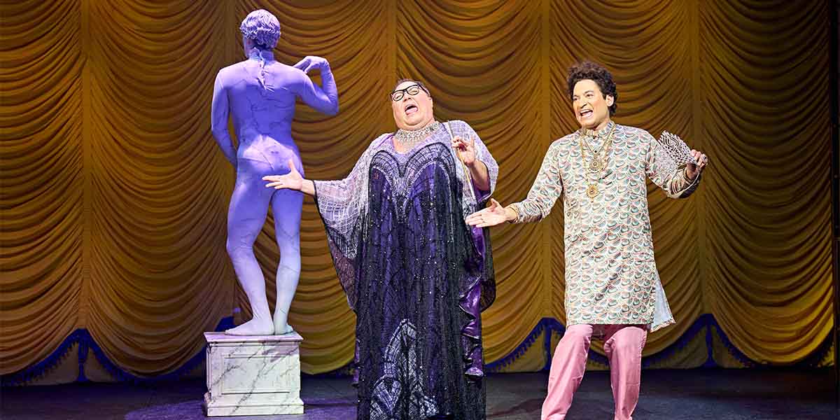 Trevor Ashley as Roger DeBris and Raj Ghatak as Carmen Ghia perform on stage, with a statue behind them.