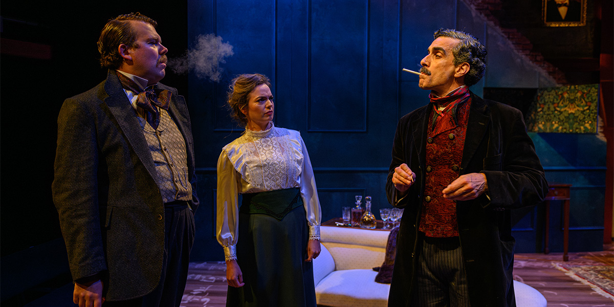 Three actors performing on stage in a Victorian-era setting, with one character smoking a cigarette and the other two attentively observing.