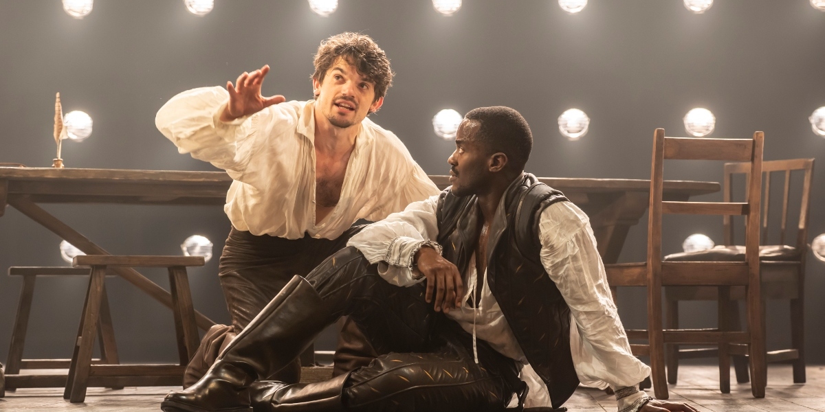 Edward Bleumel and Ncuti Gatwa pose together, smiling, against a soft-focus background with warm lighting.