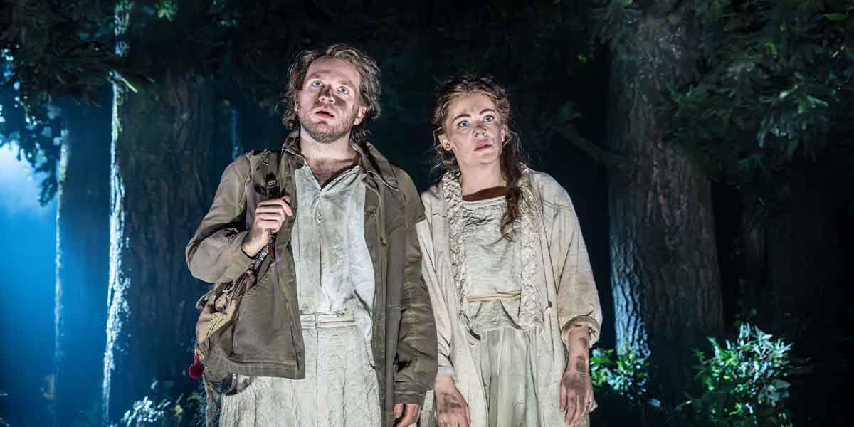 Hughie O'Donnell and Rachel Tucker stand together, looking surprised, in a dimly lit forest setting.