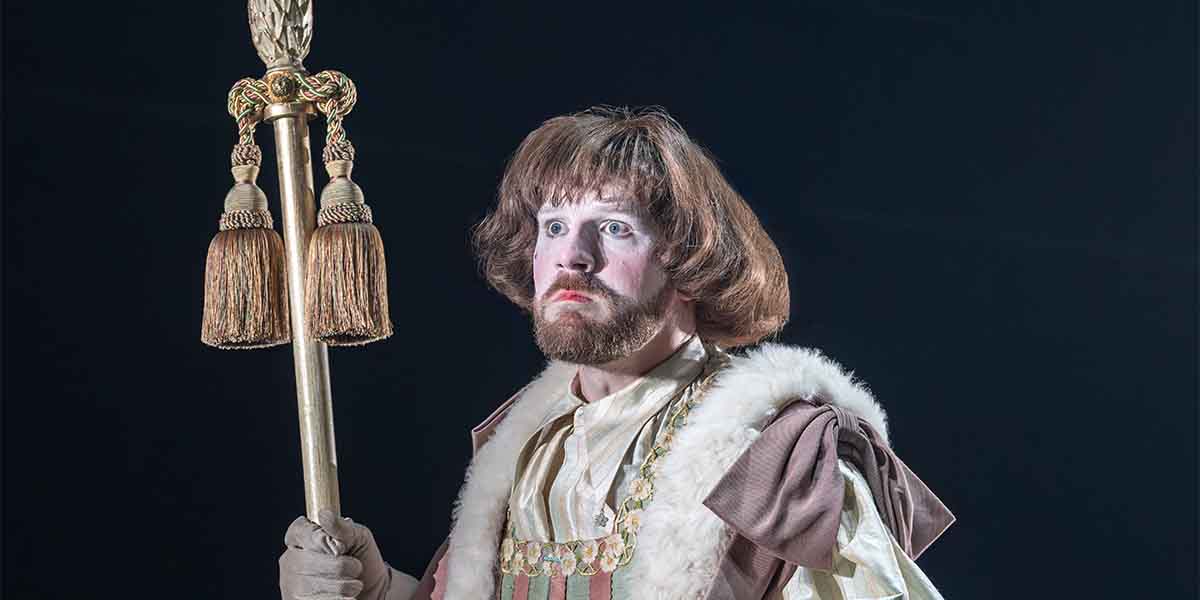 Jack Quarton, in elaborate costume with a staff, poses dramatically against a dark background.