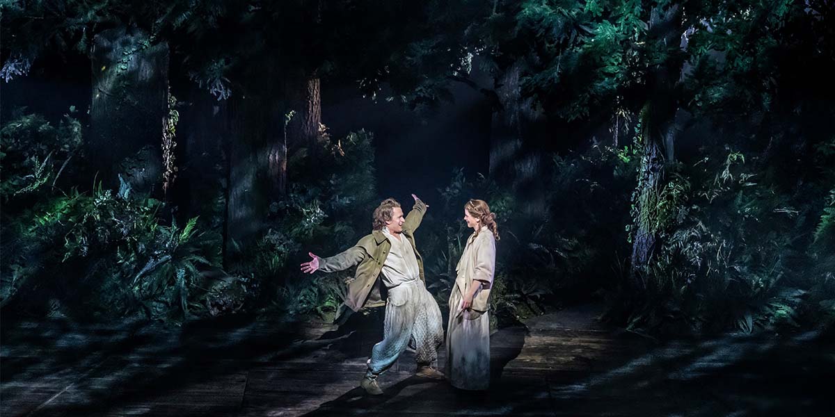 Jamie Parker and Katie Brayben smiling together, dressed in casual attire, with a blurred outdoor background.