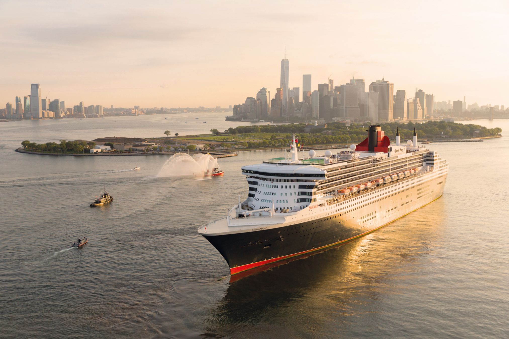 A large cruise ship approaches a city skyline during a warm golden hour.