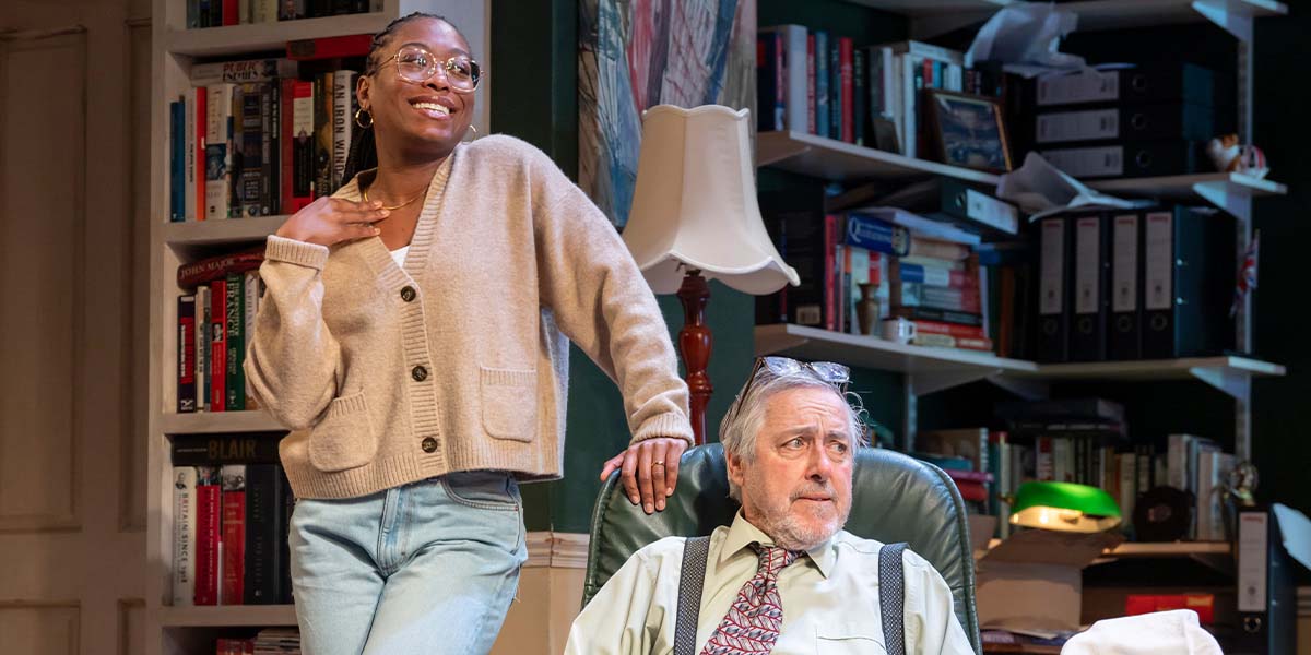 A group of people, including a woman in a blue dress, stands in a formal setting, discussing.