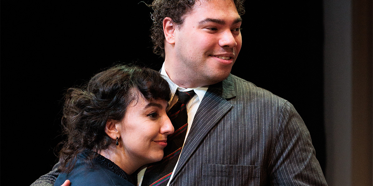 Ailsa Joy and Daniel Abbot pose together, smiling, against a textured background, with warm lighting.