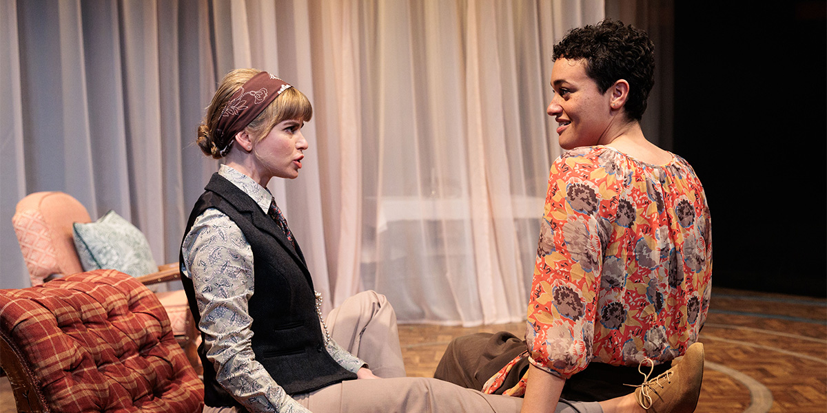 Gina Bramhill and Lily Nichol sit together on a sofa smiling, in a well-lit setting with soft textures.