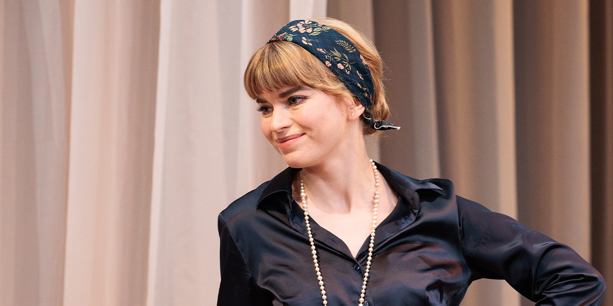 Gina Bramhill poses confidently, smiling, with soft lighting highlighting her features against a blurred background.