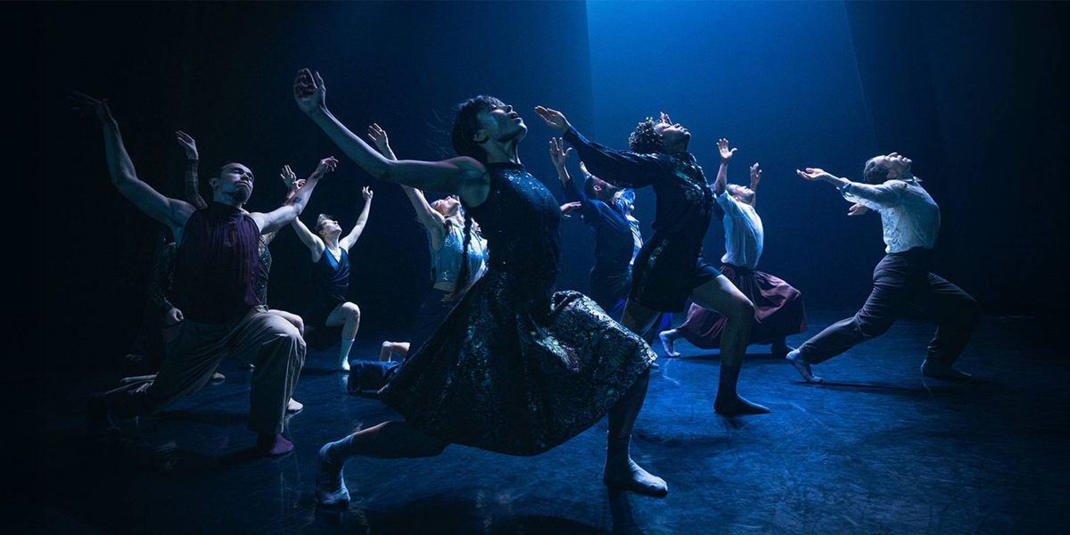 A group of dancers performing a contemporary piece on a dimly lit stage, elegantly posed with expressions of passion and intensity.
