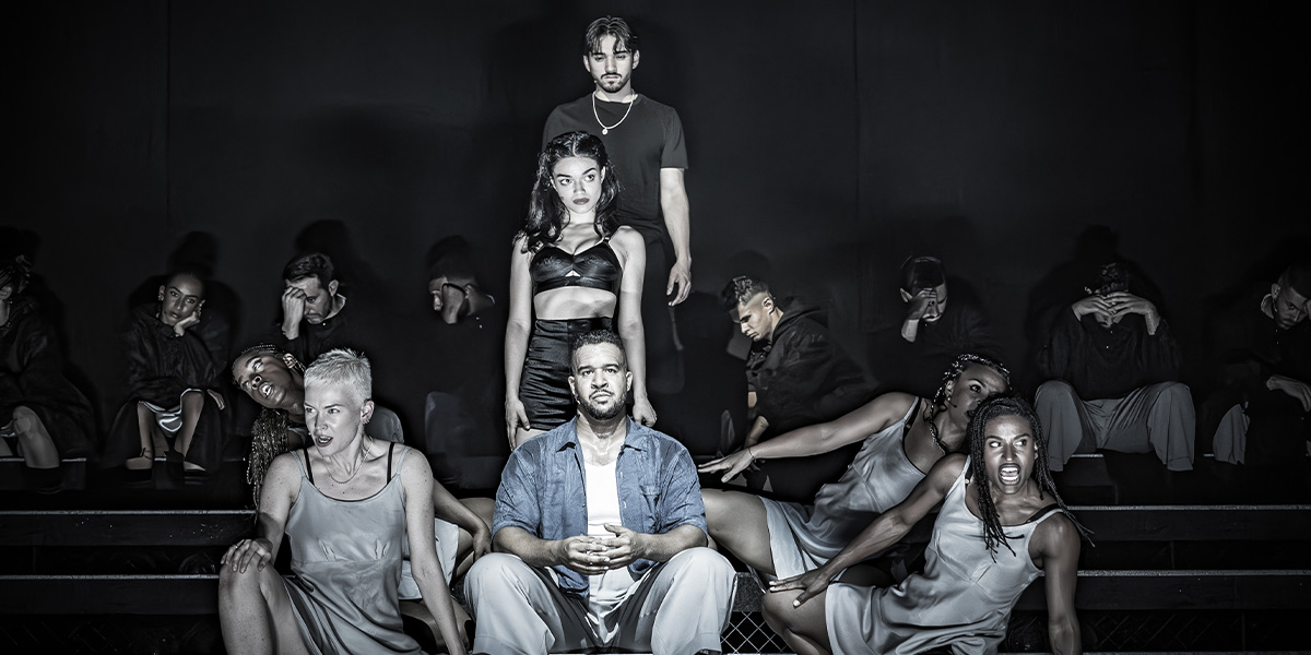 Group of eight performers posing dramatically in a modern, monochrome setting, showing varying expressions and styles.