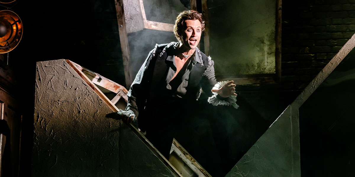 Person descending dramatically on a wooden staircase under stage lighting, expressing surprise or fear, in a theatrical setting reminiscent of a horror or mystery play.