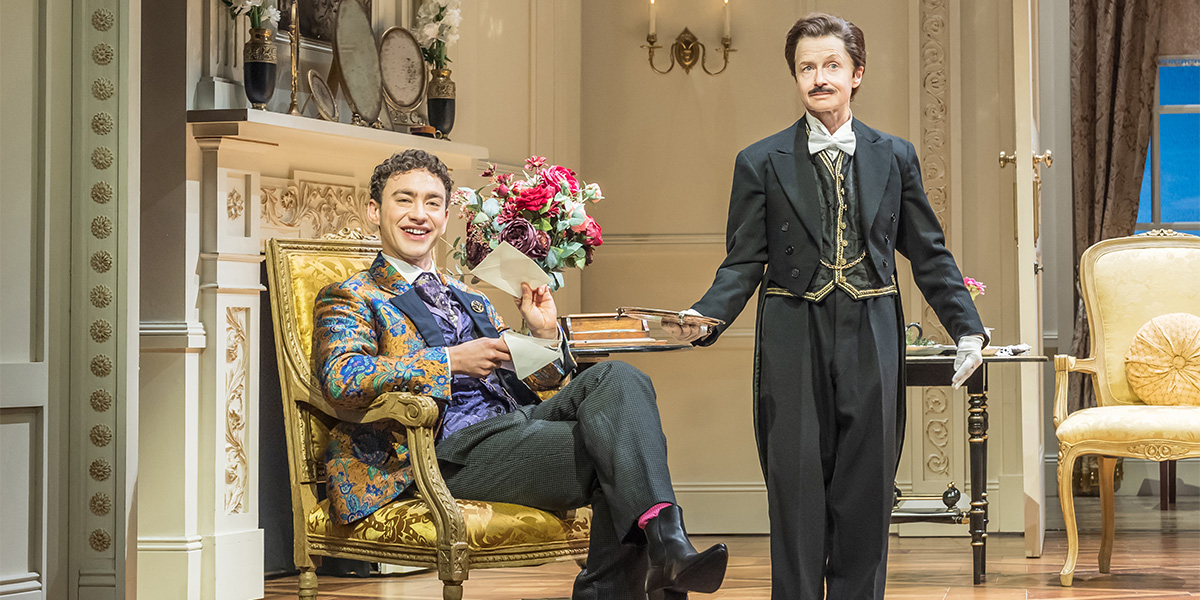 Olly Alexander and Hayley Carmichael perform on stage, dressed in period costumes, with a theatrical backdrop.
