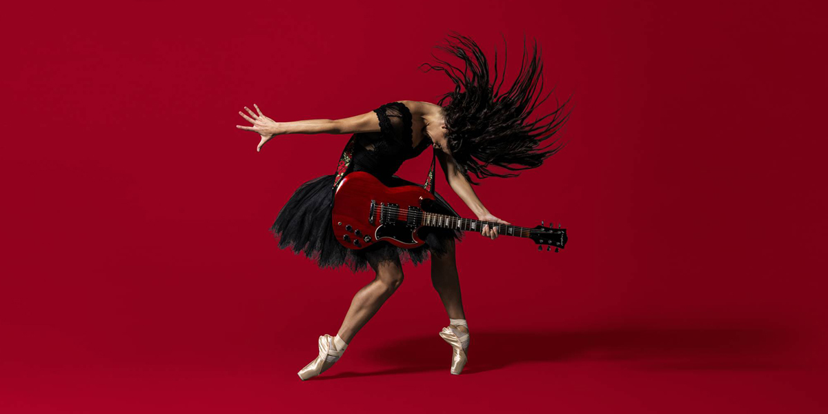 The background is red. In the centre a person can be seen wearing a black tutu and playing a red, electric guitar. The person is wearing pink ballet shoes and is standing en pointe.