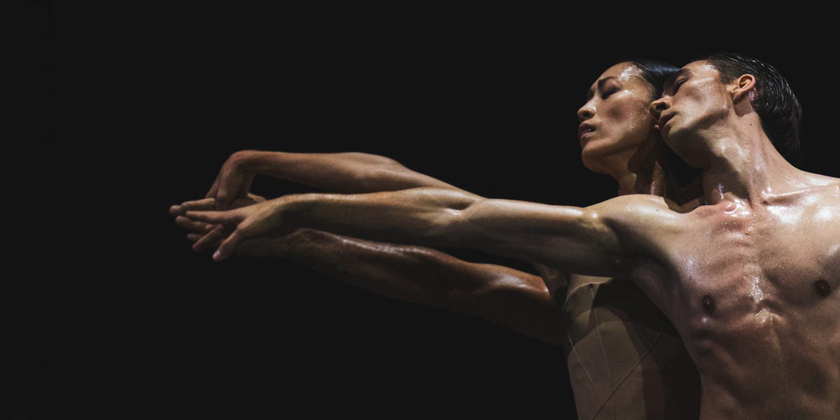 The background is black. On the right is an image of two dancers stretching out in front of them in an intimate pose.