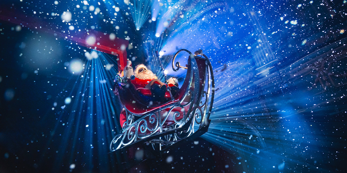 Martyn Ellis, dressed as Santa, smiles warmly in a festive red suit with white trim, surrounded by holiday decorations.