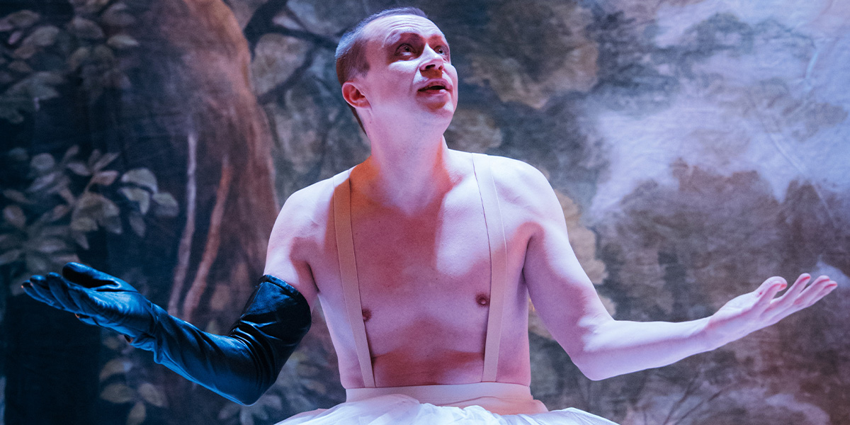 Sergo Vares as Puck, wearing a green costume with leaves, performs on stage at Shakespeare's Globe.