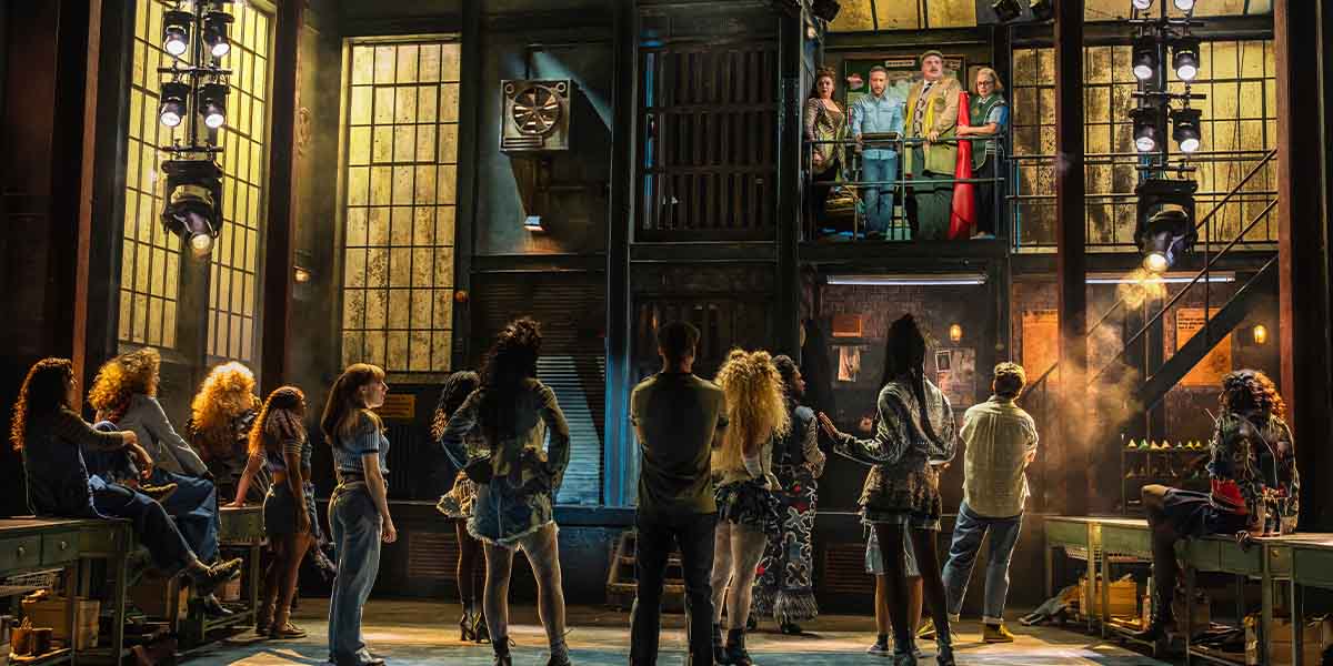 The cast of Kinky Boots poses together, wearing vibrant costumes with bold colours and playful expressions.