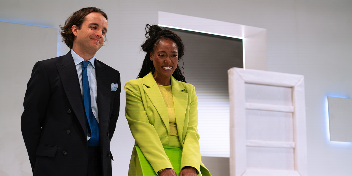 Two actors in period costumes, Arsema Thomas in blue and Keelan Kember in brown, against a textured backdrop.