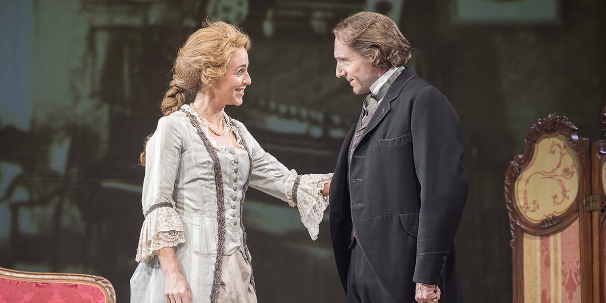 Miranda Raison as Ellen Terry and Ralph Fiennes as Henry Irving interact warmly on stage, dressed in period costumes.