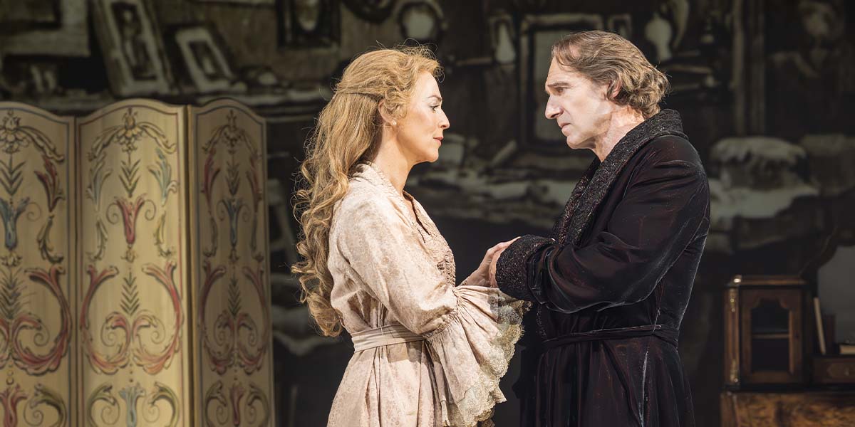 Miranda Raison as Ellen Terry and Ralph Fiennes as Henry Irving in period costumes on stage.