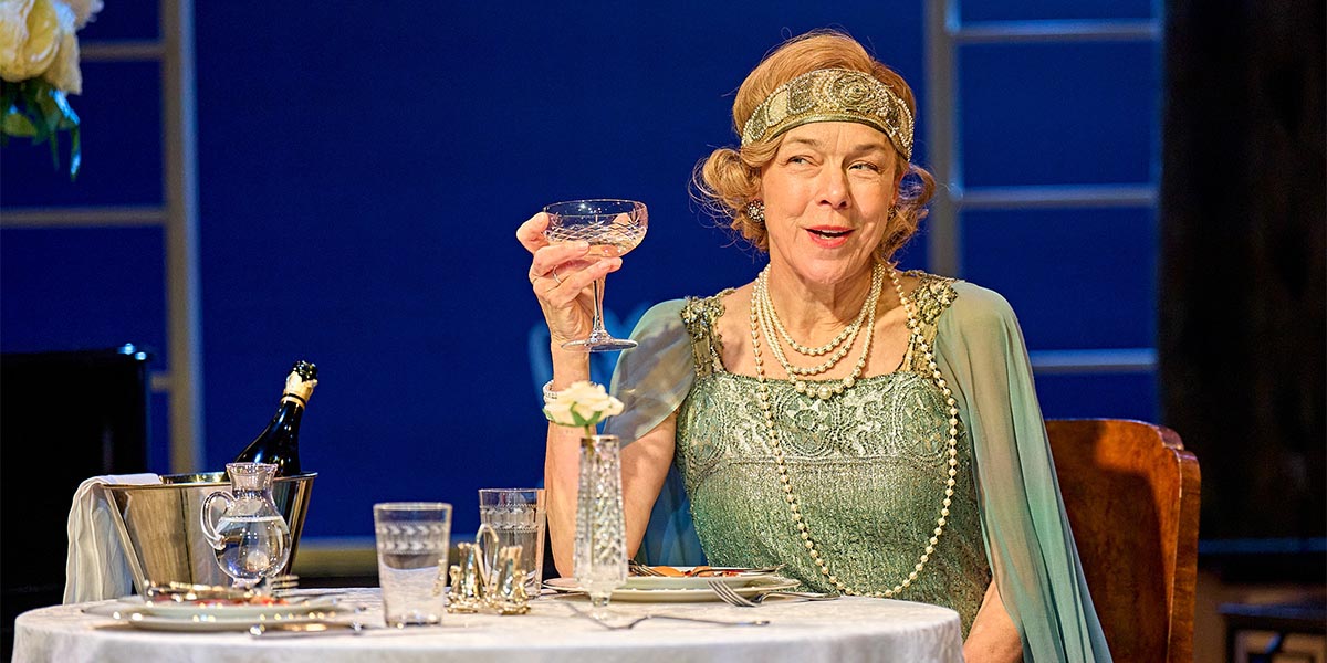 Janie Dee and Julia Steroll perform on stage, dressed in elegant costumes, with dramatic lighting and a dark background.