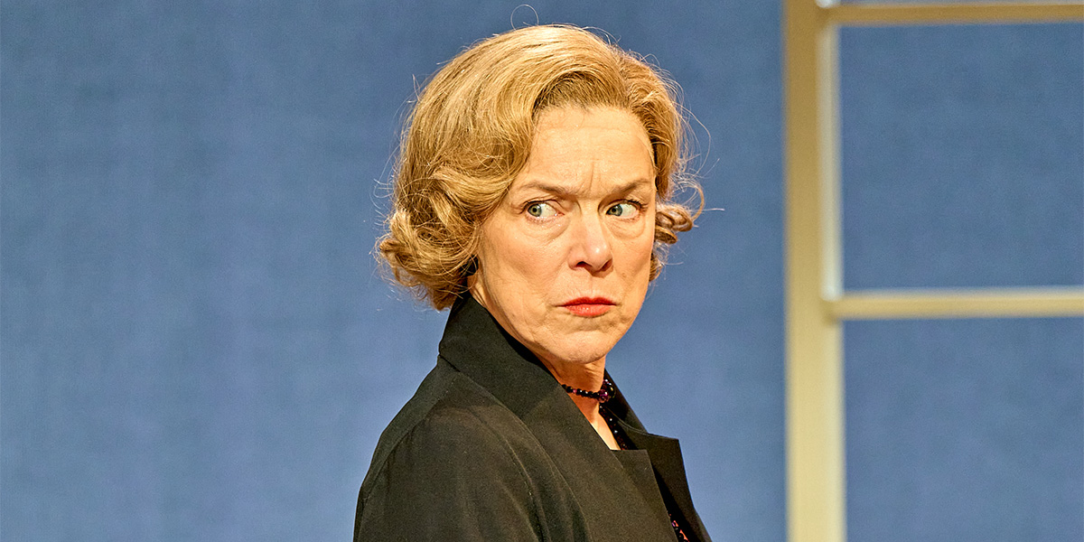 Janie Dee as Julia Steroll, wearing a flowing dress, stands on stage with dramatic lighting.