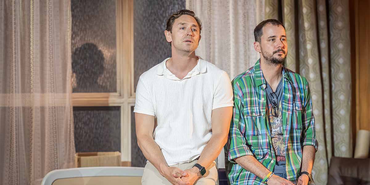 JJ Feild and Sam Swainsbury sit side by side, looking contemplative, against a softly lit backdrop.