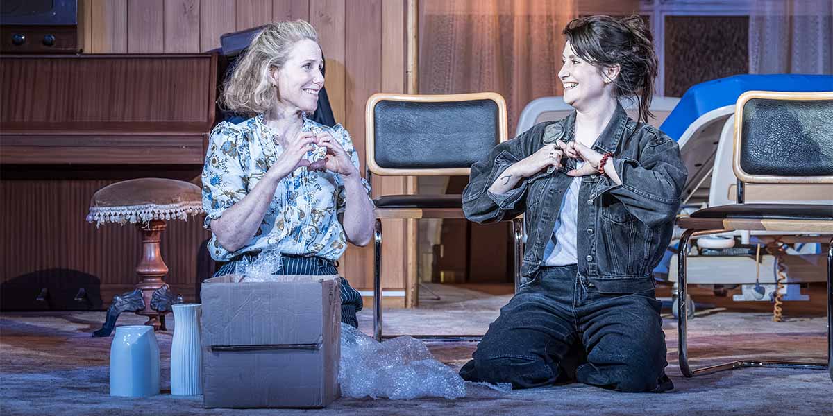Sally Phillips and Charly Clive pose together, smiling, in a brightly lit setting with soft textures.