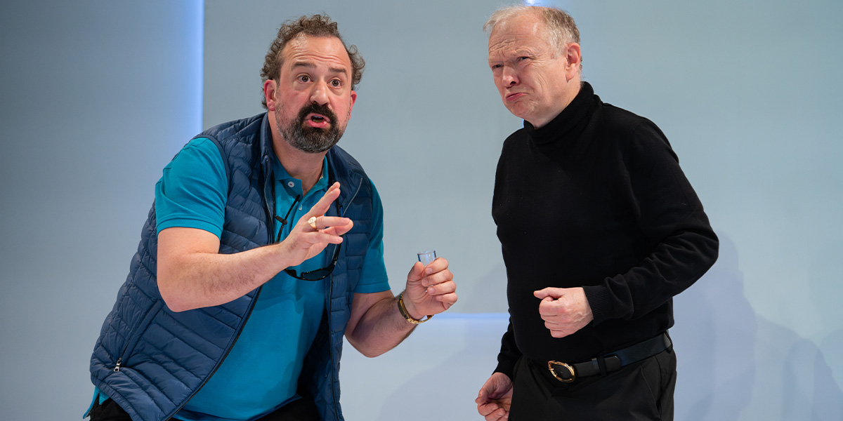 Steve Zissis and John Albasiny smiling, wearing casual clothes, against a soft-focus urban background.