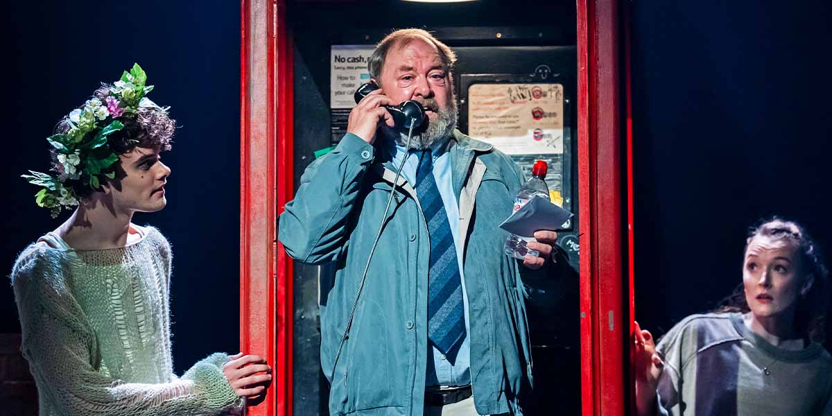 Noah Mullins as The Balladeer, Mark Addy as Harold Fry, and Nell Martin in ensemble costumes on stage.