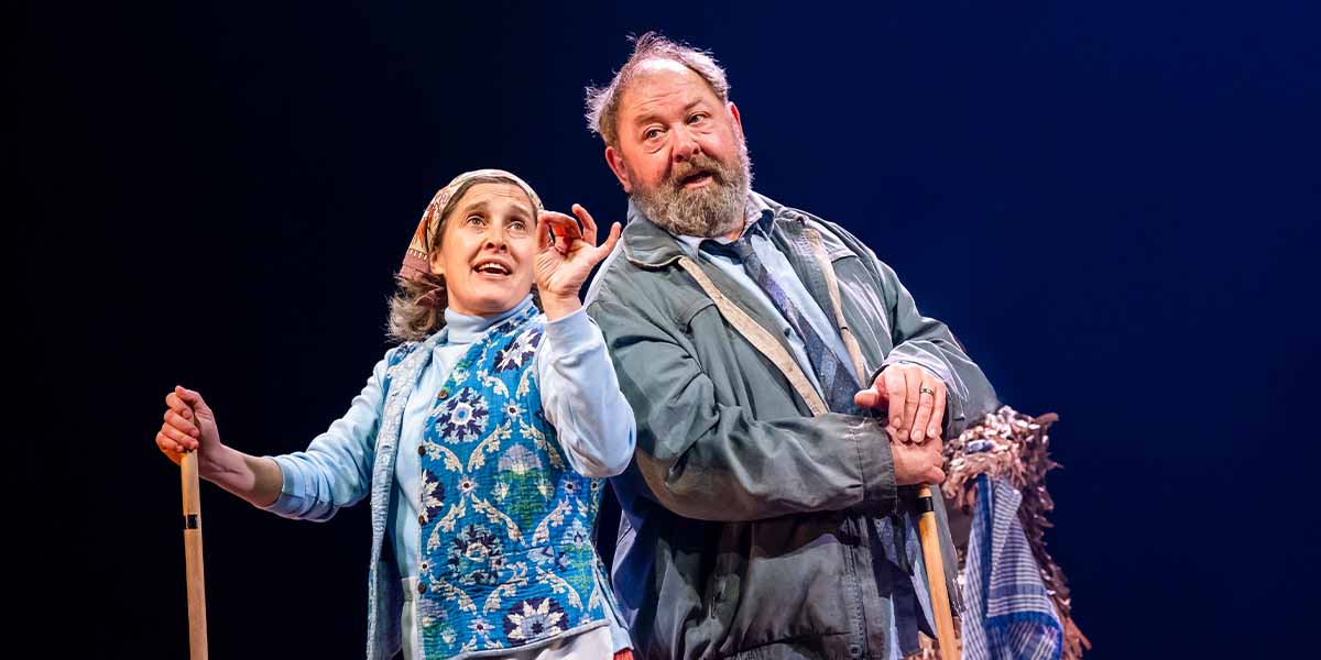 Madeleine Worrall and Mark Addy perform on stage, expressing emotion with gestures against a dark background.