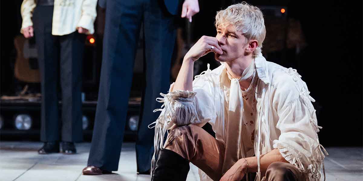 Roman Asde sits thoughtfully, dressed in a frayed white shirt and brown trousers, with two figures behind.