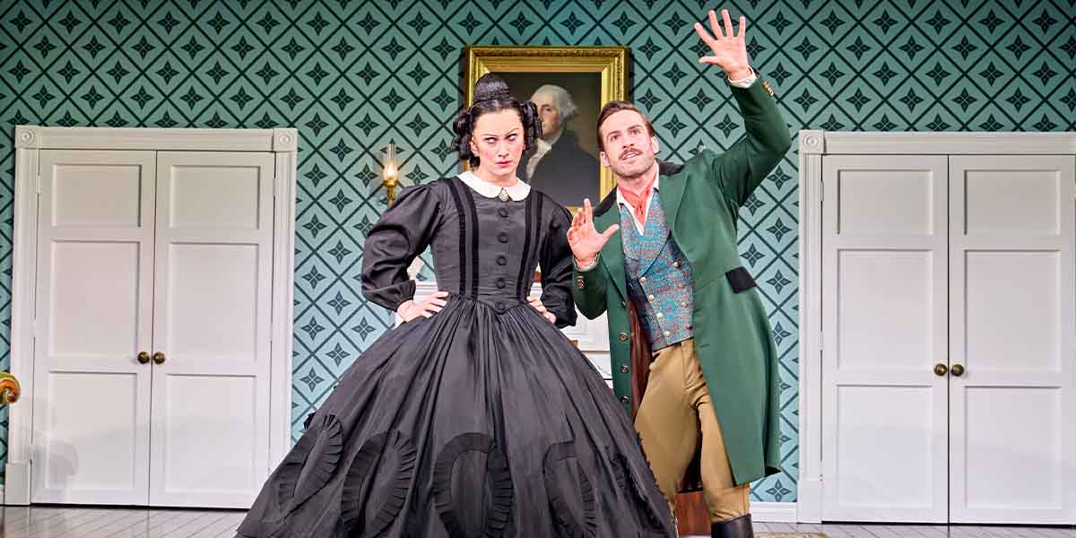 Jinkx Monsoon as Mary Todd Lincoln and Dino Fetscher as Mary's Teacher pose in a theatrical setting.