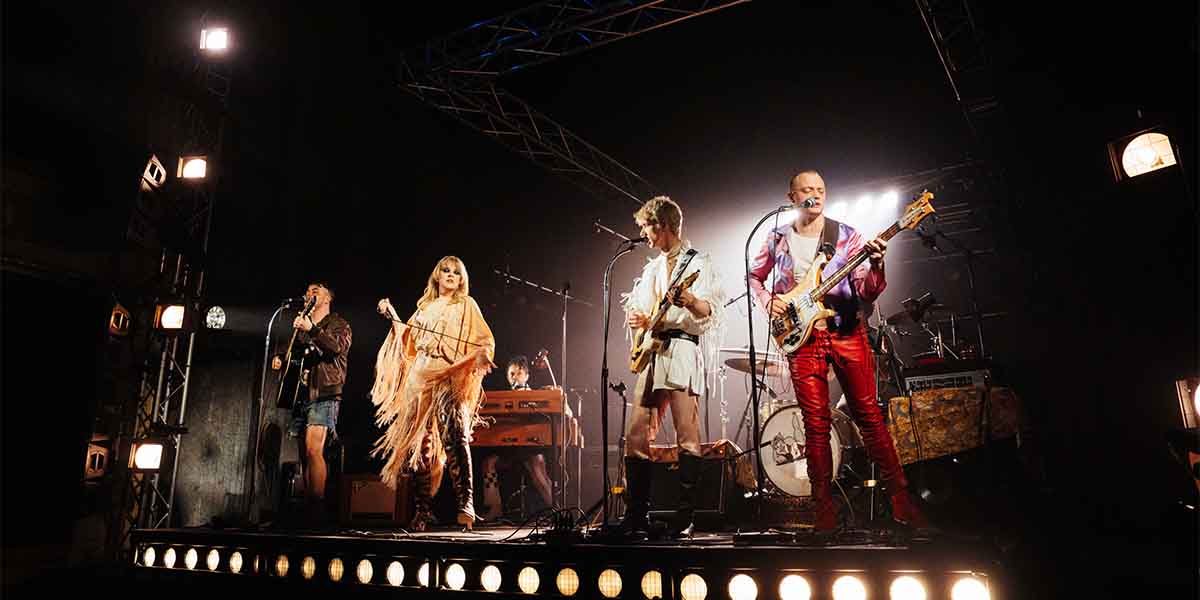 Noah Weatherby, Rebecca Lucy Taylor, Samuel Jordan, and Jojo Macari perform on stage with instruments.