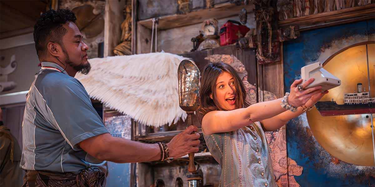 A man holds a shiny object while a woman playfully poses with a camera, smiling.