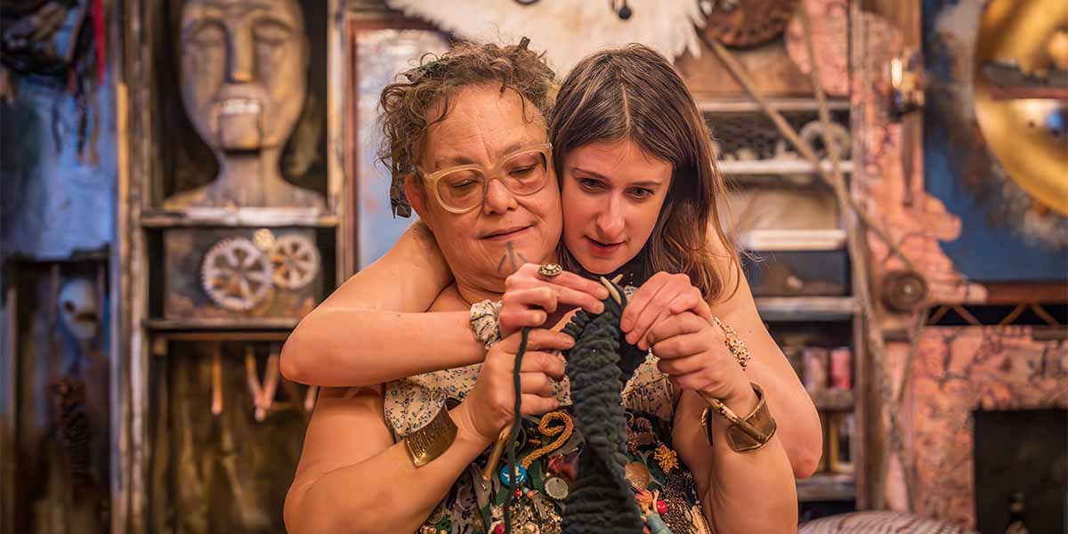 Two women closely knit together, with one guiding the other's hands, surrounded by a textured, artistic background.