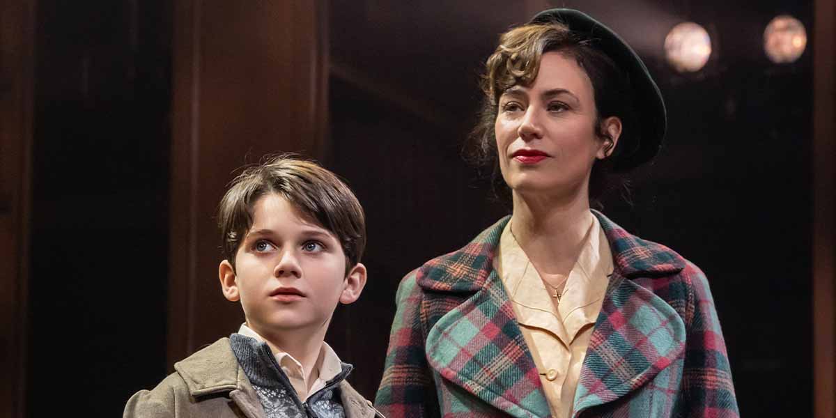 A young boy and a woman stand together, both looking upwards, with warm lighting and wooden background.