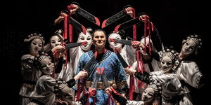 A close-up of a vibrant red flower with green leaves, set against a blurred natural background.