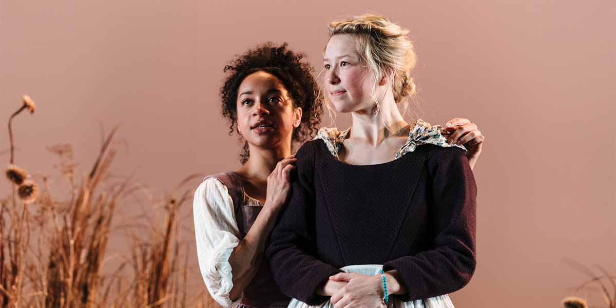 Two people stand together, one with curly hair in a white dress, the other in a dark dress.