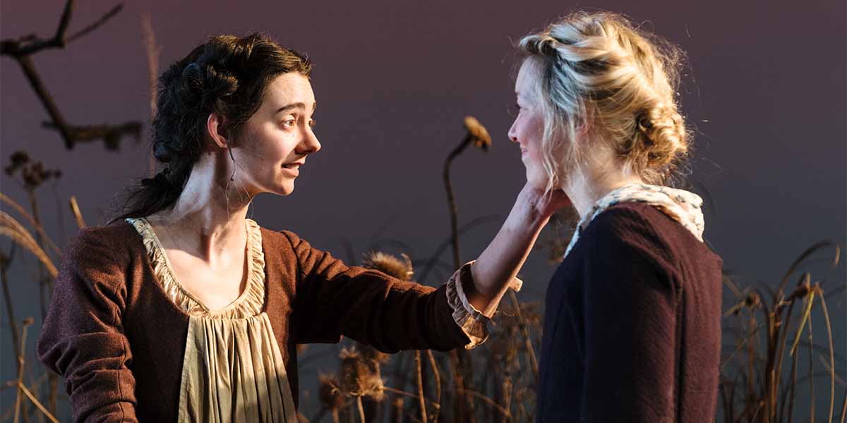 Two people interact closely, one touching the other's face, surrounded by soft lighting and natural elements.