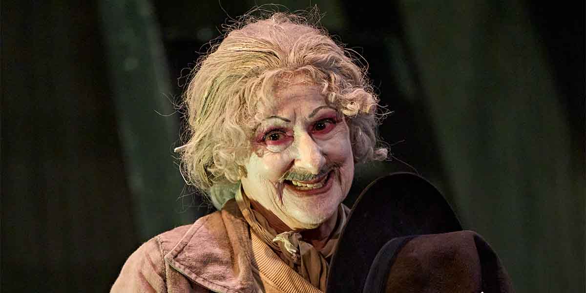 Evelyn Krape as The Figure smiles, wearing a vintage outfit with curly hair and dramatic makeup.