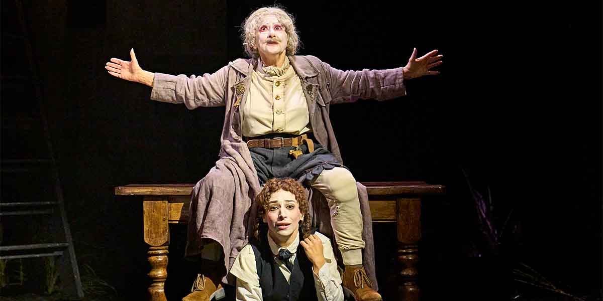 Evelyn Krape as The Figure sits on a table, arms outstretched, while Amy Hack as Yentl looks up.