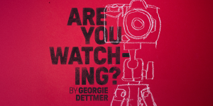 A person sits on a couch, intently watching a television screen in a dimly lit room.