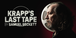 A man sits at a desk, listening to a tape recorder, surrounded by dim lighting and cluttered papers.