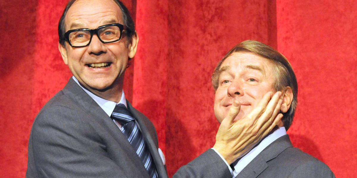Close-up of Eric holding Ern's face, both smiling against a red curtain background. 